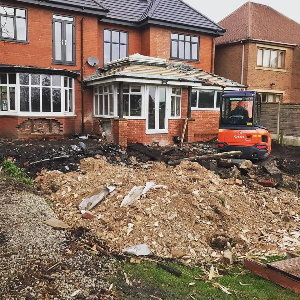 A bulldozer digging through a pile of rubble in front of a house.